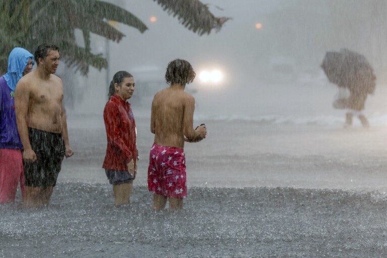 People try to cross a flooded street in Miami Beach, Fla., Wednesday, June 12, 2024.  (AP via Al Diaz/Miami Herald)