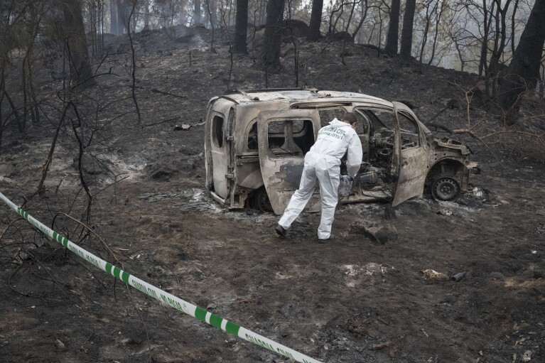 A police scientist inspects the remains of the car where two women died after a wildfire in Pontevedra, in the northwestern Spanish region of Galicia, Spain, Monday, Oct. 16, 2017. (AP Photo/Lalo R. Villar)