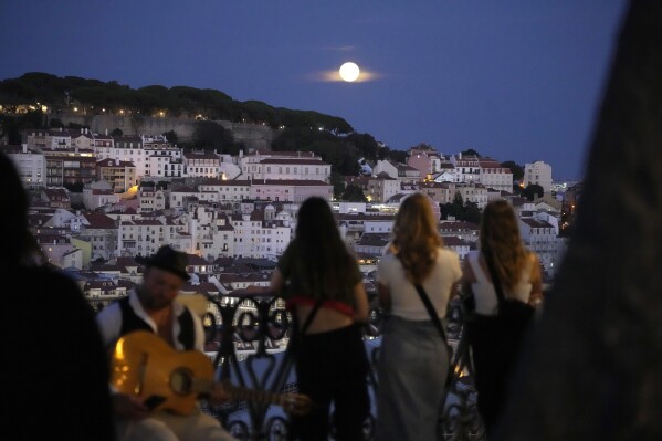 People watch a supermoon rise above Lisbon, Wednesday, Aug. 30, 2023. (AP Photo/Armando Franca)