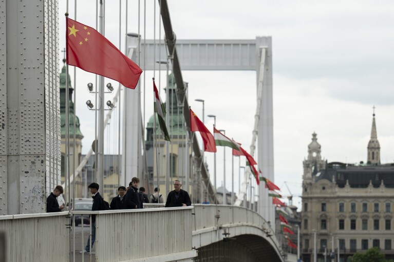 FILE - Tourists stand under Chinese and Hungarian national flags placed on the Elisabeth Bridge in Budapest, Hungary, Wednesday, May 8, 2024. Most countries in the European Union are making efforts to “de-risk” their economies from perceived threats posed by China. But Hungary and Serbia have gone in the other direction. They are courting major Chinese investments in the belief that the world’s second-largest economy is essential for Europe’s future. (AP Photo/Denes Erdos, File)