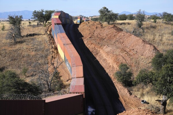 FILE - A long row of double-stacked shipping contrainers provide a new wall between the United States and Mexico in the remote section area of San Rafael Valley, Ariz., Thursday, Dec. 8, 2022. Two federal lawsuits filed over former Arizona Gov. Doug Ducey’s decision last year to place thousands of shipping containers along the U.S.-Mexico border have been dismissed after the state said it would pay the U.S. Forest Service $2.1 million to repair environmental damage. The Sept. 15, 2023, dismissal of the cases in U.S. District Court ends the fight over the double-stacked containers that were placed as a makeshift border wall. (AP Photo/Ross D. Franklin, File)