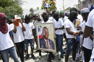 Members of the gang led by Jimmy Cherizier, alias Barbecue, a former police officer who heads a gang coalition known as "G9 Family and Allies," carry a photo of slain President Jovenel Moise during a march to demand justice for his murder, in La Saline neighborhood of Port-au-Prince, Haiti, Monday, July 26, 2021. Moise was assassinated on July 7 at his home. (AP Photo/Matias Delacroix)