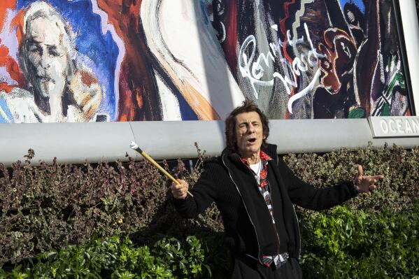 British musician and painter Ronnie Wood poses for photographers with a paintbrush after signing his name, at a photo call to unveil his new artwork entitled 'Abstract Performance' at Wood Lane, west London on Tuesday, Feb. 1, 2022. (Photo by Joel C Ryan/Invision/AP)