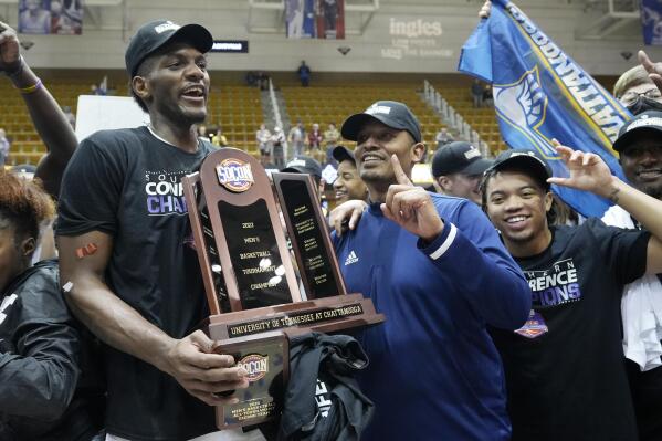 Chattanooga forward Silvio De Sousa, left, and head coach Lamont Paris hold the championship trophy to celebrate their win over Furman in an NCAA college basketball championship game for the Southern Conference tournament, Monday, March 7, 2022, in Asheville, N.C. (AP Photo/Kathy Kmonicek