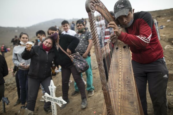 Harpist and cemetery worker Charlie Juarez performs while Gregoria Zumaeta, 44, left, mourns the death of her brothers Jorge Zumaeta, 50, and Miguel Zumaeta, 54, who died from COVID-19, at the Nueva Esperanza cemetery on the outskirts of Lima, Peru, Tuesday, May 26, 2020. (AP Photo/Rodrigo Abd)