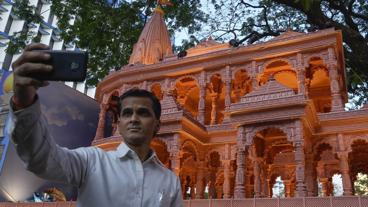 A person takes selfie in front of a replica of the Lord Ram temple in Ayodhya, which is on display outside India's ruling Bharatiya Janata Party office, in Mumbai, India, Tuesday, Jan. 16, 2024. (AP Photo/Rafiq Maqbool)
