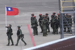 FILE - A Taiwanese soldier holds a Taiwan national flag near a group of soldiers with red markings on their helmets to play the role of an enemy during the annual Han Kuang military exercises simulating an attack on an airfield at Taoyuan International Airport in Taoyuan, Northern Taiwan, July 26, 2023. The Biden administration has approved a new $500 million arms sale to Taiwan as it ramps up military assistance to the island despite fervent objections from China. (AP Photo/Chiang Ying-ying, File)