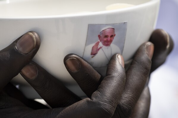 A priest holds a sacrament bowl showing a photograph of Pope Francis at a Holy Mass at the John Garang Mausoleum in Juba, South Sudan Sunday, Feb. 5, 2023. Pope Francis is in South Sudan on the final day of a six-day trip that started in Congo, hoping to bring comfort and encouragement to two countries that have been riven by poverty, conflicts and what he calls a "colonialist mentality" that has exploited Africa for centuries. (AP Photo/Ben Curtis)