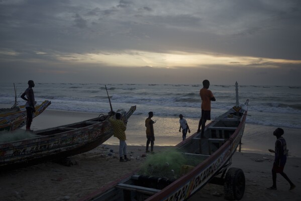 FILE - Senegalese youth gather around pirogues on the beach at dusk in Fass Boye, Senegal, Aug. 29, 2023. Officials in Senegal say at least two dozen people have died off Senegal’s northern coast and many were injured when a boat carrying migrants capsized. The boat was bound for Europe and capsized Wednesday, Feb. 28, 2024 near the town of Saint-Louis where bodies washed up on shore. (AP Photo/Felipe Dana, File)