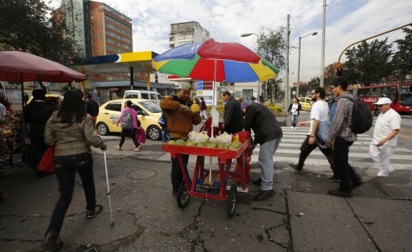 
              In this June 9, 2017 photo, Venezuelans Jesus Barrios and Wilson Bernadette park their cart at a busy intersection to sell mangoes, in Bogota, Colombia. Many of the Venezuelans arriving today have Colombian roots, but those who do not find gaining legal status difficult. Unlike nearby Peru, which offers Venezuelan arrivals temporary work visas, Colombia does not provide any sort of humanitarian legal status to Venezuelans. Refugee visas are available but can take more than two years to process. (AP Photo/Fernando Vergara)
            