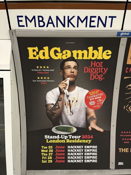 A view of a poster advertising comedian Ed Gamble's Hot Diggity Dog tour on the Bakerloo line platform at Embankment underground station in London, Wednesday March 27, 2024. Gamble has been ordered to change a subway station poster campaign for his new standup show because the image of a hot dog violated the transit network’s ban on junk food advertising. The poster for the show, “Hot Diggity Dog,” showed a mustard- and ketchup-smeared Gamble beside a half-eaten hot dog on a plate. A bemused Gamble replaced the wiener with a cucumber, and the poster was approved. (Joe Sene/PA via AP)