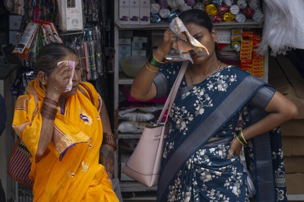 Women wipe the sweat from their faces as they wait for bus on a hot and humid summer day in Mumbai, India, Thursday, May 23, 2024. (AP Photo/Rafiq Maqbool)
