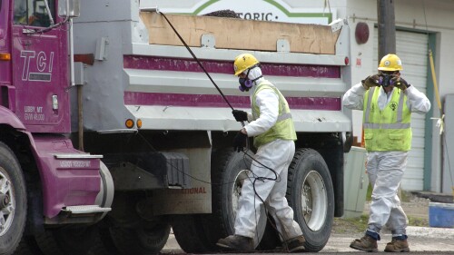 DOSSIER - Des ouvriers routiers non identifiés portent un équipement de protection contre une éventuelle contamination par l'amiante lorsqu'ils chargent des matériaux provenant d'un projet de resurfaçage de routes dans le centre-ville de Libby, dans le Montana, le 28 avril 2011. Une clinique de santé dans la ville du Montana qui est en proie à une contamination mortelle par l'amiante est passible de près de 6 millions de dollars en pénalités et dommages après avoir soumis des centaines de fausses demandes de prestations gouvernementales.  (AP Photo/Matthew Brown, Fichier)