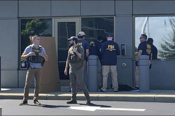 In this image taken from FOX19 Cincinnati video, FBI officials gather outside the FBI building in Cincinnati, Thursday, Aug. 11, 2022. An armed man decked out in body armor tried to breach a security screening area at the FBI field office in Ohio on Thursday, then fled and exchanged gunfire in a standoff with law enforcement, authorities said. (FOX19 Cincinnati via AP)