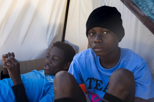 Eduardo Afonso, 15, and Makiese Alexandria Shabani, 10, both of Angola, sit in the shade of a tent at an encampment of asylum-seekers mostly from Venezuela, Congo and Angola next to an unused motel owned by the county, Wednesday, June 5, 2024, in Kent, Washington. The group of about 240 asylum-seekers is asking to use the motel as temporary housing while they look for jobs and longer-term accommodations. (AP Photo/Lindsey Wasson)