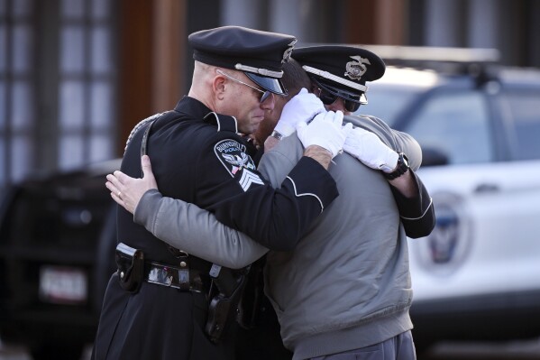 Taylor Jacobs, center, who was with Burnsville Police for 10 years, embraced members of the department's honor guard Tuesday, Feb. 20, 2024 outside the Ballad-Sunder Funeral and Cremation in Jordan, Minn. Two young police officers and a firefighter-paramedic were killed in a burst of gunfire Sunday as they responded to a domestic disturbance call in the Minneapolis suburb of Burnsville. Another officer also was injured, and the man identified as the shooter fatally shot himself, police said. (Aaron Lavinsky/Star Tribune via AP)