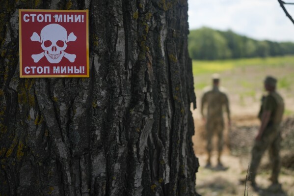 A notice warning about land mines is attached to a tree as a Ukrainian specialized team searches for mines in a field in the outskirts of Kyiv, Ukraine, Thursday, June 9, 2022. (AP Photo/Natacha Pisarenko)