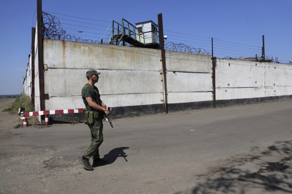 FILE - A soldier stands guard next to a wall of a prison in Olenivka, in an area controlled by Russian-backed separatist forces, eastern Ukraine, July 29, 2022. A Russian news agency is reporting that the country is preparing to send a battalion of Ukrainian prisoners of war to the front lines in their homeland to fight on Moscow's side in the war. The Associated Press could not immediately confirm the authenticity of the report or if the POWs were coerced. (AP Photo, File)