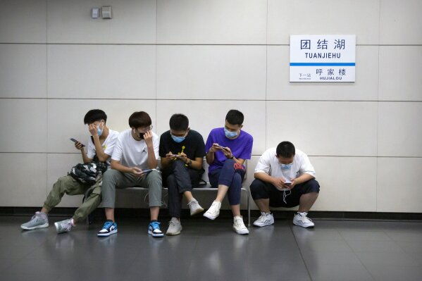 People wearing face masks to protect against the coronavirus sit on a bench in a subway station in Beijing, Friday, July 17, 2020. Further restrictions are being imposed on the northwestern Chinese city of Urumqi following a cluster of new cases. (AP Photo/Mark Schiefelbein)