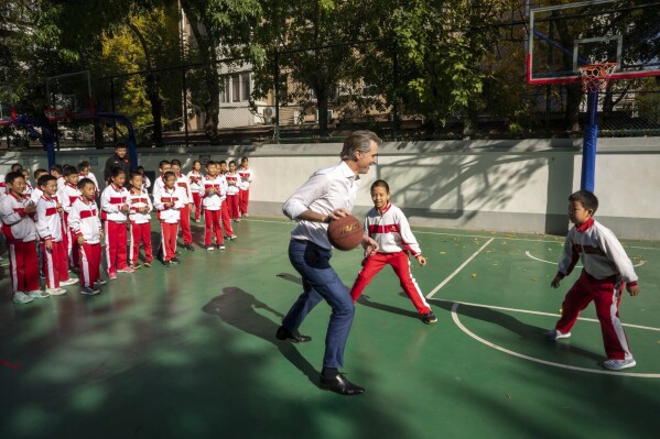 In this photo provided by the Office of the Governor of California, Gov. Gavin Newsom plays basketball with children at a school in Beijing, Friday Oct. 27, 2023. (Courtesy of Office of the Governor of California via AP)