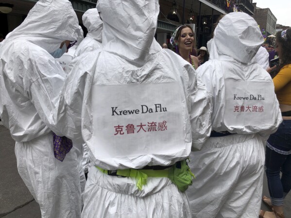 Mardi Gras revelers sport hazmat suits in a spoof of epidemic scares, Feb. 25, 2020, on Bourbon Street in New Orleans. (AP Photo/Kevin McGill, file)