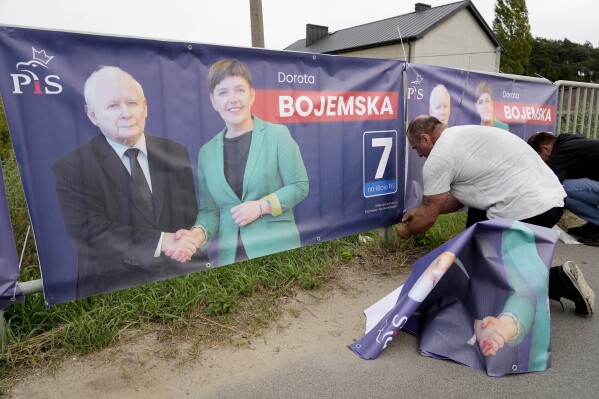 A man puts up election banners for a candidate of the ruling conservative Law and Justice party, including an image of the party leader and Poland's de-facto leader Jaroslaw Kaczynski, in Czosnow near Warsaw, on Wednesday, Oct. 11, 2023. The Poles are voting in key parliamentary elections on Sunday that will decide whether Law and Justice wins a third consecutive term, or the pro-European opposition forms the new government. AP Photo/Czarek Sokolowski)