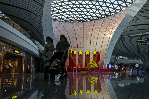 Travelers walk by a Communist Party's logo decorated at the departure hall of Beijing Daxing International Airport, in Beijing on Oct. 24, 2023. China's leaders are expected to search for ways to mend the country's fractured property market, create jobs for millions of unemployed youths and spur faster growth in a meeting that reportedly began Monday, Oct. 30 in Beijing. (AP Photo/Andy Wong)