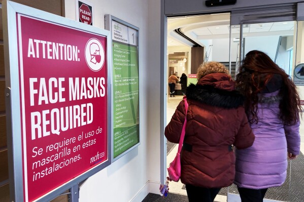 A sign announcing a face mask requirement is displayed at a hospital in Buffalo Grove, Ill., Friday, Jan. 13, 2023. COVID-19 hospital admissions are inching upward in the United States since early July 2023. It's a small-scale echo of the three previous summers. (AP Photo/Nam Y. Huh)