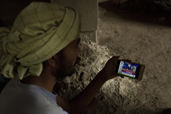 FILE- An Indian laborer at a building construction site watches election trends on a mobile phone in Gauhati, India, May 23, 2019. Misinformation about India's election is surging online as the world's most populous country votes. The country has a huge online ecosystem, with the largest number of WhatsApp and YouTube users in the world. (AP Photo/Anupam Nath, File)