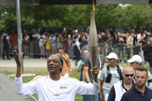 Snoop Dogg carries the Olympic torch at the 2024 Summer Olympics, Friday, July 26, 2024, in Saint-Denis, outside Paris, France. (AP Photo/Aurelien Morissard)