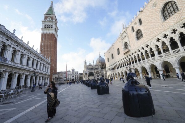 A visitor walks next to the "Las Meninas a San Marco" sculptures part of the installation by the Spanish artist Manolo Valdés, at the San Marco's Square during the 60th Biennale of Arts exhibition in Venice, Italy, Tuesday, April 16, 2024. The Venice Biennale contemporary art exhibition opens Saturday for its six-month run through Nov. 26. (AP Photo/Luca Bruno)