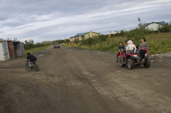 Children ride on an ATV vehicle on Phillips street, Friday, Aug. 18, 2023, in Akiachak, Alaska. Many villagers prefer ATV vehicles for transportation due to widespread potholes. (AP Photo/Tom Brenner)
