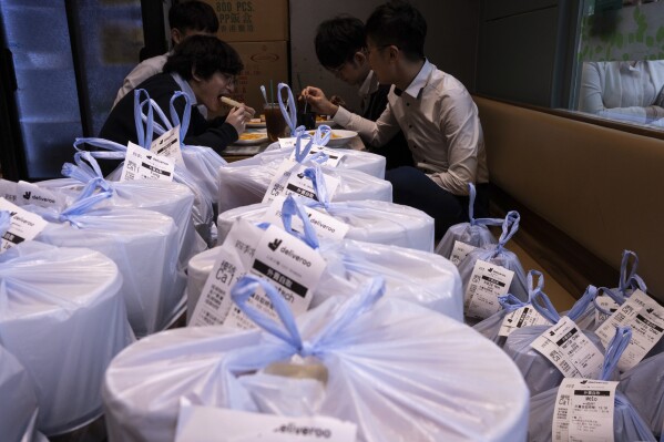 Customers eat lunch next to takeaway food plastic bags ready for pick up at a restaurant in Hong Kong, Thursday, Feb. 21, 2024. Hong Kong has long been a major producer and consumer of great food, and a great amount of plastic and Styrofoam to go with it. That’s going to change as new legislation aiming to stop the sale and distribution of Styrofoam products and single-use plastic cutlery went into effect on Monday, April 22, 2024.(AP Photo/Louise Delmotte)