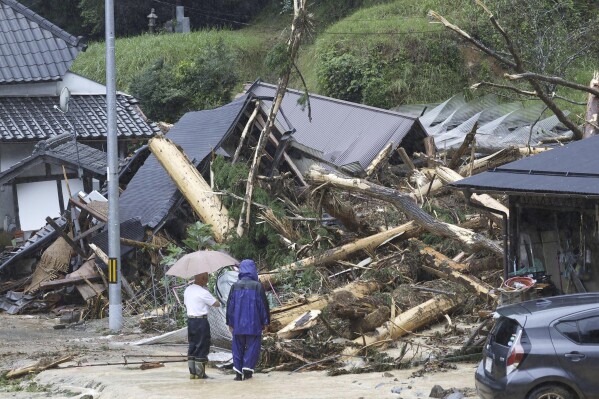 People stand by a mudslide site following a storm in Ayabe, Kyoto prefecture, western Japan Tuesday, Aug. 15, 2023. A strong tropical storm lashed central and western Japan with heavy rain and high winds Tuesday, causing flooding and power blackouts and paralyzing air and ground transportation while many people were traveling for a Buddhist holiday week. (Kyodo News via AP)