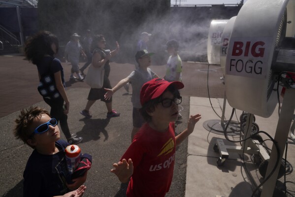Brothers Henry Peters, 6, left, and Charles Peters, 8, cool off in misting fans at the USTA Billie Jean King National Tennis Center in New York, Tuesday, Aug. 22, 2023. (AP Photo/Seth Wenig)