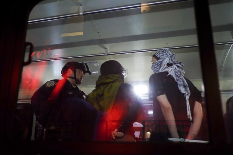 Members of the New York City Police Department's Strategic Response Team load an arrested Columbia University protester onto a bus, Tuesday, April 30, 2024, in New York City. After entering campus, a squad of police officers approached Hamilton Hall, the administrative building that student demonstrators had begun occupying in the morning.  (AP Photo/Julius Mortal)