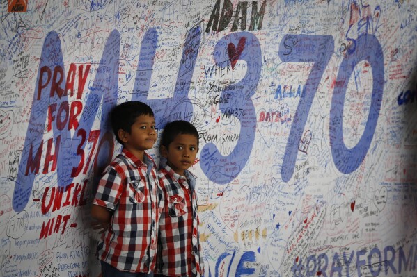 FILE - Two Malaysian children stand in front of a messages board and well wishes on it to people involved with the missing Malaysia Airlines jetliner MH370, in Sepang, Malaysia, on March 16, 2014. A decade ago this week, a Malaysia Airlines flight vanished without a trace to become one of aviation’s biggest mystery. Investigators still do not know exactly what happened to the plane and its 239 passengers. (AP Photo/Vincent Thian, File)