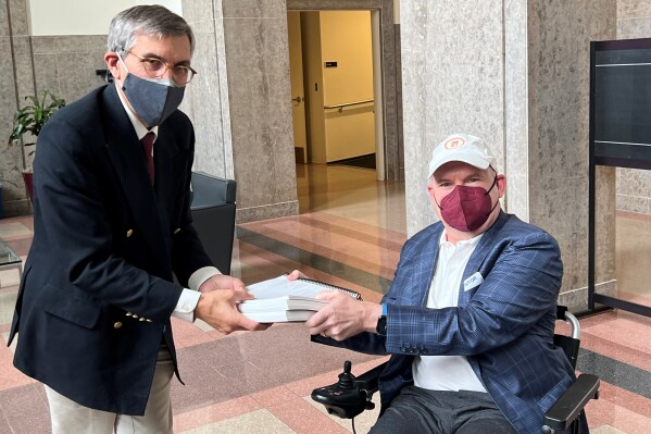 En esta fotografía proporcionada por la organización de pacientes con esclerosis lateral amiotrófica I AM ALS, Dan Tate, a la derecha, entrega una petición impresa al doctor Peter Marks, director del centro de productos biológicos de la Administración de Alimentos y Medicamentos de EEUU (FDA), para que aprueben nuevos tratamientos contra la ELA, en el campus de la FDA en Silver Spring, Maryland, el 14 de diciembre de 2022. (Sonya Elling/I AM ALS vía AP)