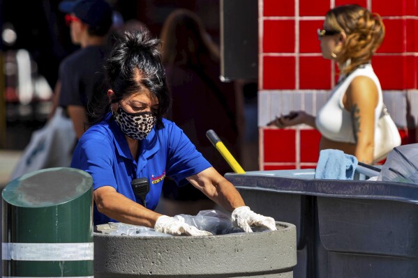 A maintenance worker empties trash bins, Friday, Aug. 25, 2023, in Las Vegas. A historic heat wave that began blasting the Southwest and other parts of the country this summer is shining a spotlight on one of the harshest, yet least-addressed, effects of climate change in the U.S.: the rising deaths and injuries of people who work in extreme heat, whether inside hot warehouses and kitchens or outside under the blazing sun. Many of them are migrants in low-wage jobs. (AP Photo/Ty O'Neil)