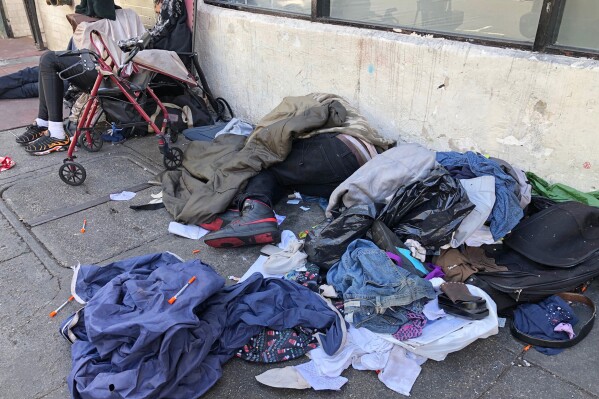 FILE - Sleeping people, discarded clothes and used needles are seen on a street in the Tenderloin neighborhood in San Francisco, July 25, 2019. The Democratic mayor of San Francisco is pushing a pair of controversial public safety proposals on the March 5, 2024, ballot. Critics say the measures are out of step with San Francisco's liberal politics and will hurt already marginalized communities. (AP Photo/Janie Har, File)