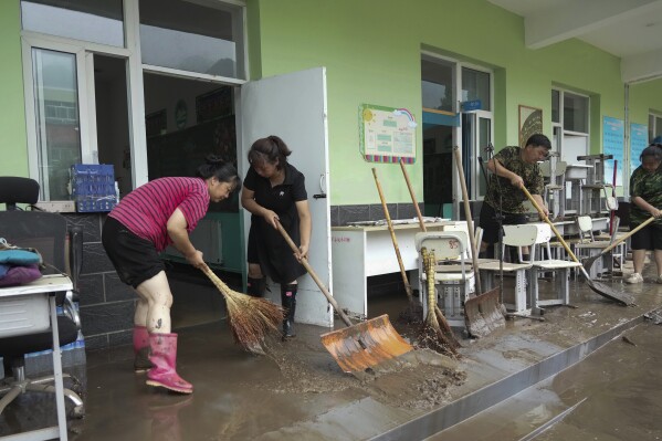 In this photo released by Xinhua News Agency, teachers clean classrooms at a school in the aftermath of flood waters from an overflowing river in Qizhongkou Town of Laishui County in north China's Hebei Province on Aug. 11, 2023. A vast swath of northeastern China is threatened by flooding as at least 90 rivers have risen above warning levels and 24 have already overflowed their banks. State media say crews are standing by to defend homes and farmland across the Songliao Basin north of Beijing which includes parts of four provinces and several major cities with a total population of almost 100 million. (Wang Kun/Xinhua via AP)