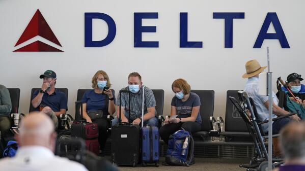 FILE - People sit under Delta sign at Salt Lake City International Airport on July 1, 2021, in Salt Lake City. Delta Air Lines won't force employees to get vaccinated, but it's going to make unvaccinated workers pay a $200 monthly charge. Delta said Wednesday, Aug. 25, 2021 that it will also require weekly testing for unvaccinated employees starting next month, although the airline says it'll pick up the cost of that testing. (AP Photo/Rick Bowmer, file)