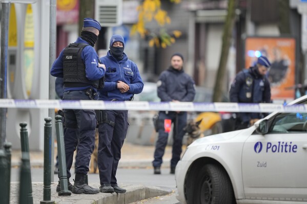 Belgian police stand behind a restricted area near the site where a suspected Tunisian militant was shot dead hours after a manhunt on Tuesday, October 17, 2023. A suspected Tunisian extremist accused of killing two Swedish soccer fans has been shot dead. He brazenly attacked on the streets of Brussels before disappearing on Monday night.  (AP Photo/Martin Meissner)