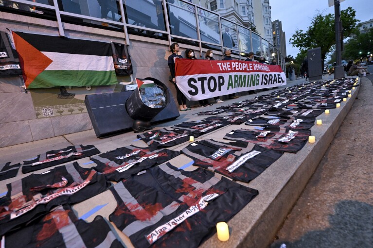 Demonstrators hold a sign while press vest lay on the ground covered in red paint during a pro-Palestinian protest over the Israel-Hamas war at the White House Correspondents' Association Dinner, Saturday April 27, 2024, in Washington. (AP Photo/Terrance Williams)