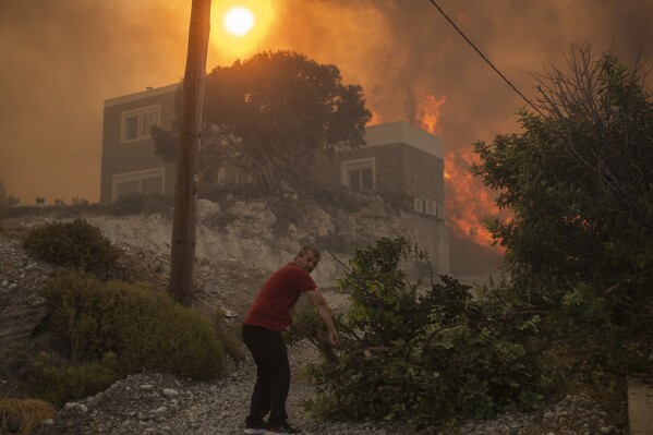 A local pulls a tree branch as a wildfire burns in Gennadi village, on the Aegean Sea island of Rhodes, southeastern Greece, on Tuesday, July 25, 2023. A firefighting plane has crashed in southern Greece, killing both crew members, as authorities are battling fires across the country amid a return of heat wave temperatures. (AP Photo/Petros Giannakouris)
