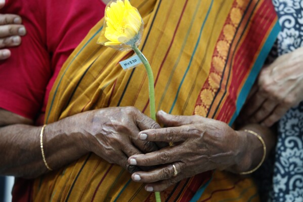 A family member of a passenger on board of the missing Malaysia Airlines Flight 370 holds a flower during the tenth annual remembrance event at a shopping mall, in Subang Jaya, outskirts of Kuala Lumpur, Malaysia, Sunday, March 3, 2024. (AP Photo/FL Wong)