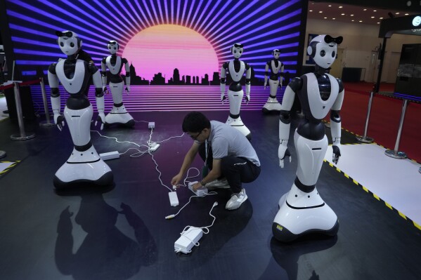 A worker charges robots displayed at the annual World Robot Conference at the Beijing Etrong International Exhibition and Convention Center in Beijing, Wednesday, Aug. 16, 2023. (AP Photo/Ng Han Guan)
