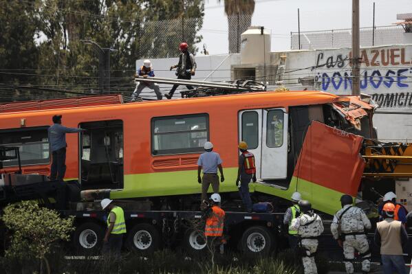 Workers remove a damaged subway car after it was lowered, with the help of a crane, to the ground from a collapsed elevated section of the metro, in Mexico City, Tuesday, May 4, 2021. The elevated section of the metro collapsed late Monday, killing at least 23 people and injuring at least 79, city officials said. (AP Photo/Marco Ugarte)