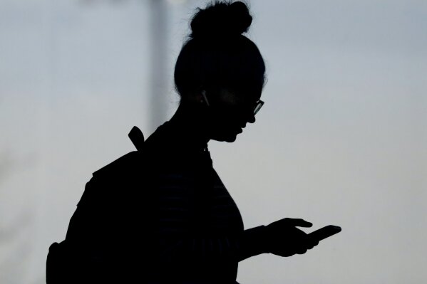 FILE - In this Nov. 14, 2019, file photo, a woman checks her phone in Orem, Utah. A new poll from The Associated Press-NORC Center for Public Affairs Research and USAFacts finds that Americans are getting information about government from social media at least as much as from traditional news sources, but few trust what they see and read. (AP Photo/Rick Bowmer, File)