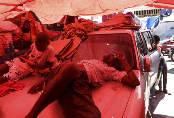 Un hombre duerme sobre un auto en un refugio para familias desplazadas por la violencia de las pandillas, en Puerto Príncipe, Haití, el 5 de junio de 2025. (AP Foto/Odelyn Joseph)